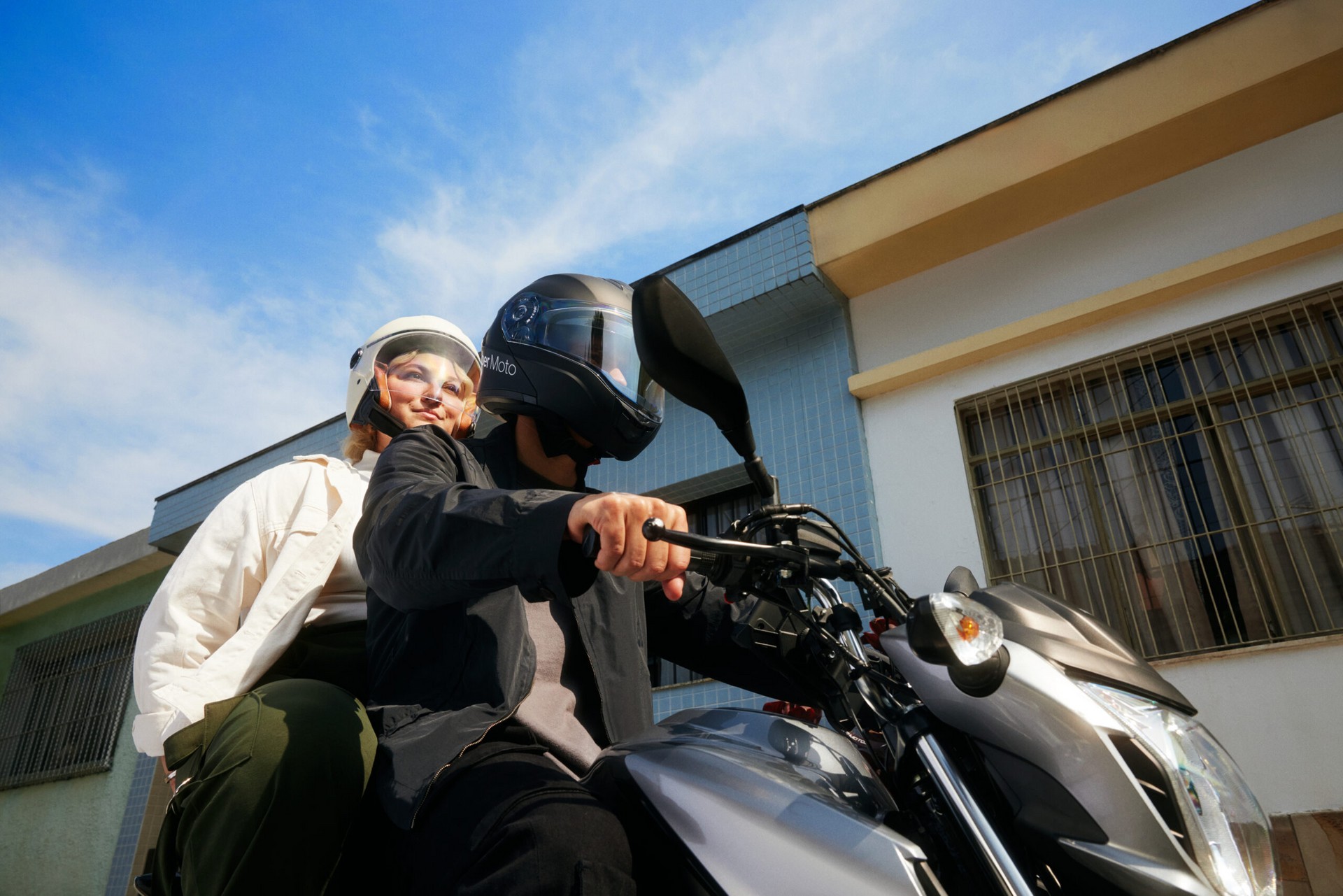 Passageira e motociclista com capacete e máscara do Uber em ponto de embarque