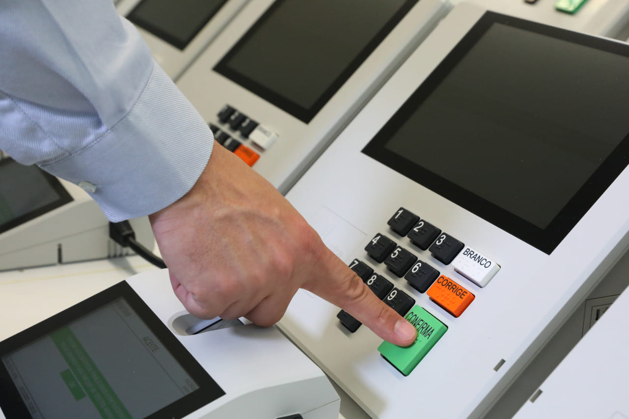 Eleitor aperta a tecla Confirma em urnas eletrônicas lado a lado
